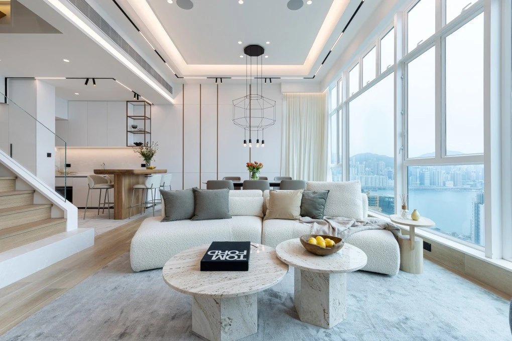 A bright, spotless living room with a white sofa, marble coffee tables, and floor-to-ceiling windows