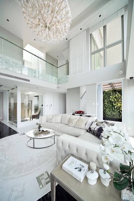 A double-height white living room with a crystal chandelier, freshly cleaned